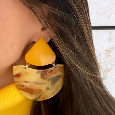 Brinco amarelo com padrão marmoreado em orelha de pessoa com cabelo castanho