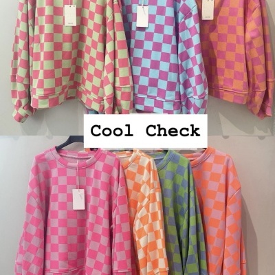 Sweatshirts coloridas com padrão de xadrez penduradas na parede com etiquetas.