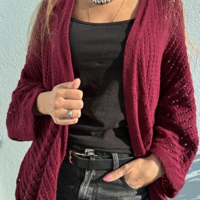 Casaco vinho de malha, camisola preta, calças jeans cinzentas e acessórios prateados em modelo