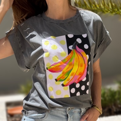 T-shirt cinzenta com estampa colorida de bananas e bolinhas, usada por pessoa com calças de ganga.