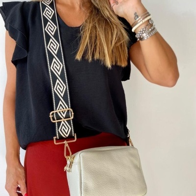 Mulher com blusa preta, calças vermelhas e bolsa de couro branco com alça preta e branca