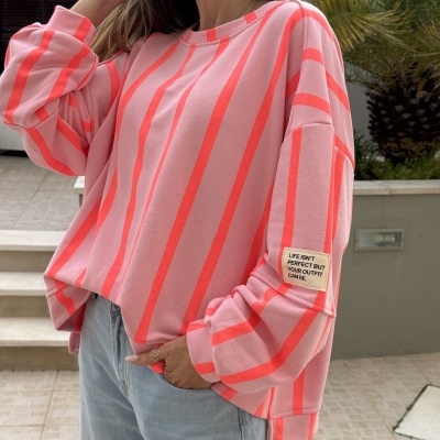 Sweatshirt rosa com riscas verticais cor de salmão e etiqueta na manga, usada com jeans azuis claros.