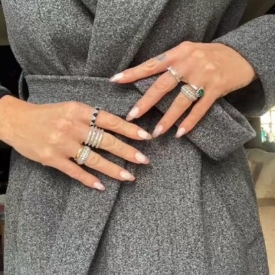 Mulher a usar casaco cinza com cinto, mãos com anéis variados.