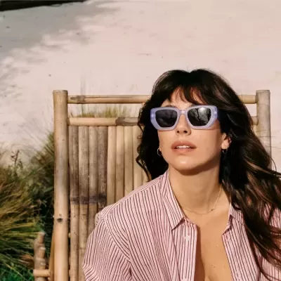 Mulher com camisa riscada e óculos de sol a sentar numa cadeira de bambu ao ar livre