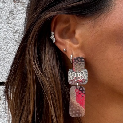 Brinco pendente metálico martelado em tons prateados e vermelhos na orelha direita