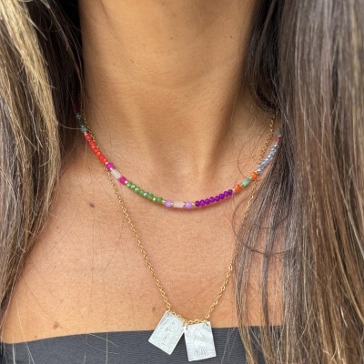 Dois colares usados no pescoço, um de miçangas coloridas e outro dourado com pendentes retangulares.