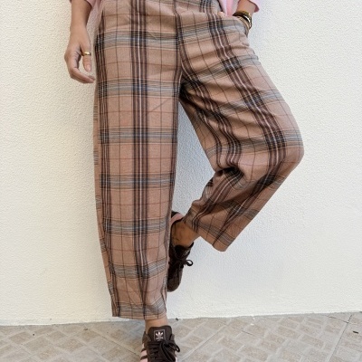 Calças largas às riscas castanho-bege-pretas com cinto castanho e ténis escuros rosa, parede branca de fundo