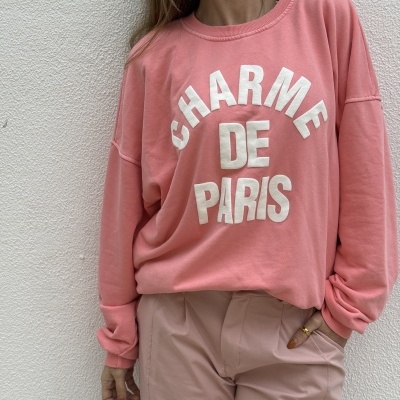Pessoa a usar sweatshirt rosa com texto branco CHARME DE PARIS, calças rosa claro, em fundo branco