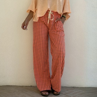 Calças largas xadrez vermelho e preto com camisa laranja clara solta e sandálias.