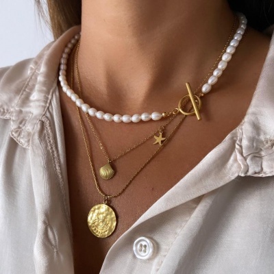 Colar triplo de pérolas naturais e correntes douradas com pingentes variados sobre camisa bege claro