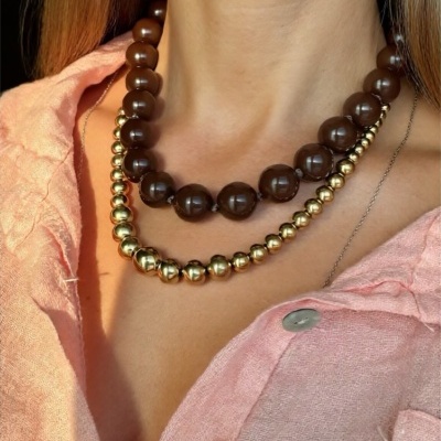 Colar duplo com contas castanhas e douradas usado sobre camisa rosa claro