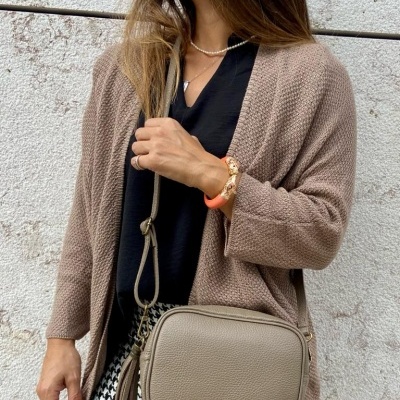 Mulher com cardigan bege, blusa preta, saia pied-de-poule, colar de pérolas, pulseira e mala bege de couro