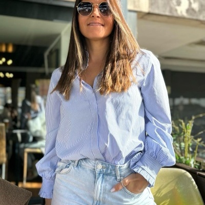 Mulher de blusa riscada azul e branca e calças de ganga azul clara com óculos de sol