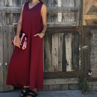 Vestido bordeaux sem mangas com clutch e sandálias pretas junto a porta de madeira