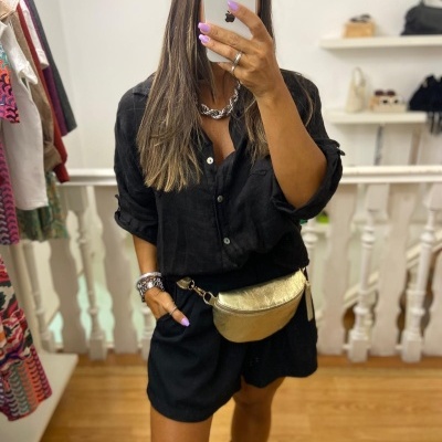 Mulher com camisa e calções pretos, botas e pochete dourada a tirar selfie num espelho