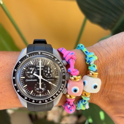 Relógio Omega Speedmaster preto com duas pulseiras coloridas de fio trançado e contas de olhos