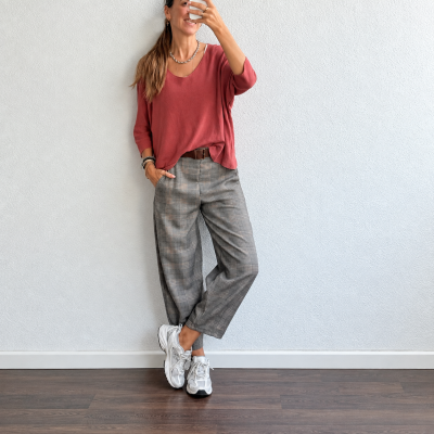 Pessoa com blusa terracota, calças xadrez cinzentas e sapatilhas brancas