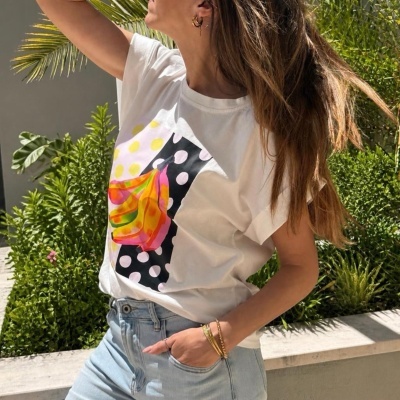Pessoa usando t-shirt branca estampada colorida e calças de ganga azul clara em ambiente exterior com plantas.