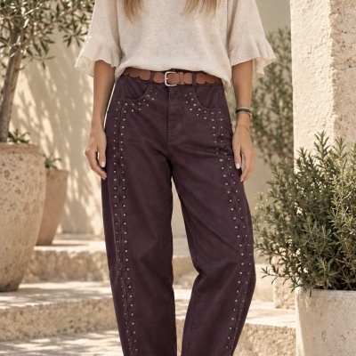 Mulher com blusa bege, calças vinho com tachas e sapatilhas branca e cinzenta ao ar livre