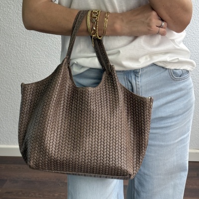 Mala castanha trançada com alças, pulseiras douradas e anéis, t-shirt branca e jeans azuis