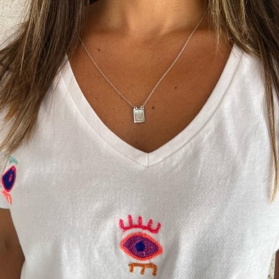 Colar prateado com pendente quadrado e t-shirt branca com bordado de olhos coloridos