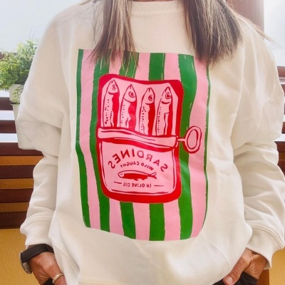 Sweatshirt creme com estampa de lata de sardinhas em cor vermelha sobre riscas verdes e rosas.