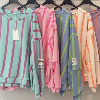 Cinco camisolas às riscas coloridas penduradas em cabides pretos com etiqueta branca com texto em preto