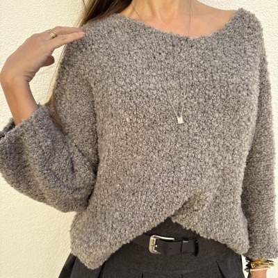 Mulher com camisola cinzenta de malha texturada e saia cinzenta escura plissada com cinto preto