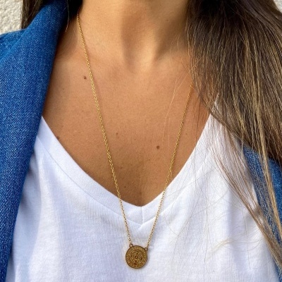 Colar dourado com pendente redondo numa pessoa com t-shirt branca com estampa de olho e coroa e casaco azul