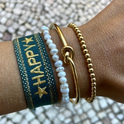 Quatro pulseiras no pulso, tecido verde com dourado, pérolas brancas, dourada com nó, contas douradas