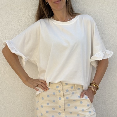 Mulher a usar t-shirt branca de mangas curtas folhadas com calças ou saia bege com bolinhas azuis.