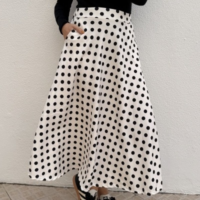 Saia midi branca com bolinhas pretas usada com camisola preta e ténis bicolores em fundo branco