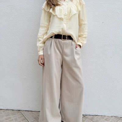 Blusa creme com folhos e bordados e calças largas bege claras com cinto preto.