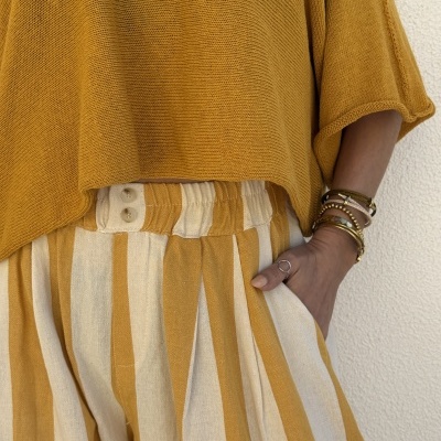 Topo amarelo mostarda de malha e calças riscas verticais amarelo e cru com botões na cintura, pulseiras no pulso.