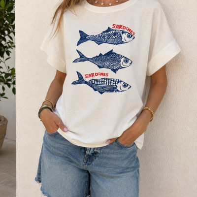 T-shirt branca com estampado de sardinhas azuis e texto vermelho, calções de ganga azuis, cenário exterior com parede branca e planta