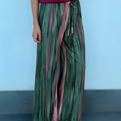 Calças largas em padrões verdes e rosa com cordão na cintura, usadas com blusa vinho e sapatos cinza.