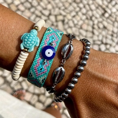 Pulseiras coloridas e metálicas num pulso com fundo de calçada de pedras pequenas