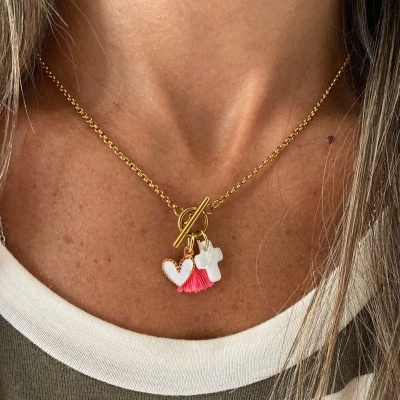 Colar dourado com pendentes de coração branco, tassel rosa e cruz branca no pescoço