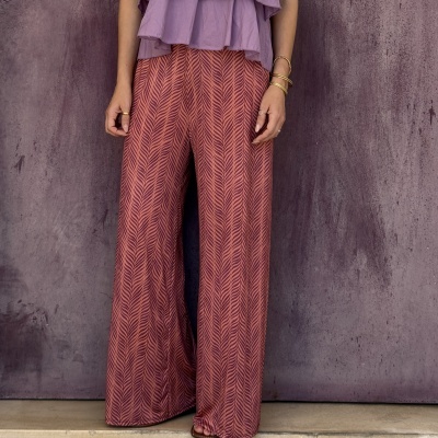 Calças largas rosa com padrão ziguezague e blusa lilás com pulseiras douradas.