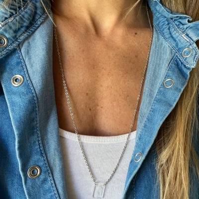 Colar prateado com pendente transparente usado sobre camisola branca e casaco azul de ganga