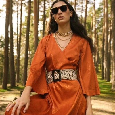 Mulher com vestido alaranjado brilhante e cinto largo estampado de cobra em floresta