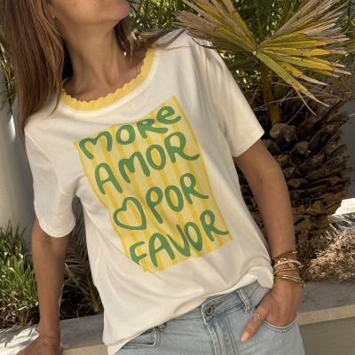 T-shirt branca com gola amarela canelada e texto verde em riscas amarelas, usada por mulher junto a plantas.