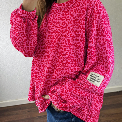 Camisola rosa com padrão animal print e etiqueta na manga, usada com calças de ganga.