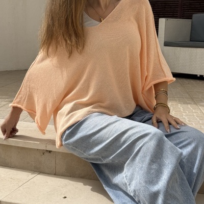 Pessoa sentada em escadas vestindo camisola pêssego de malha e calças largas de ganga azul clara