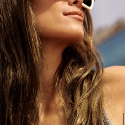 Mulher a usar óculos de sol brancos e castanhos com camisola cinza ao ar livre junto ao mar