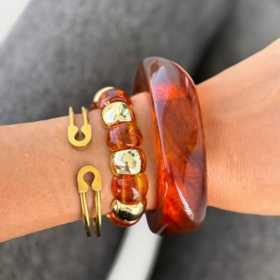 Três pulseiras, castanha translúcida, castanha com dourado e dourada minimalista, num pulso com fundo cinzento desfocado