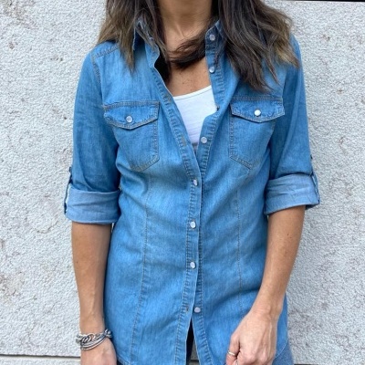 Camisa de ganga azul clara com botões e bolsos no peito, usada por mulher contra parede clara