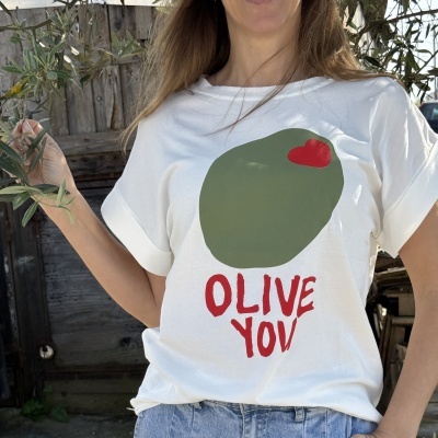 T-shirt branca com estampa verde e texto vermelho usada por pessoa ao ar livre.