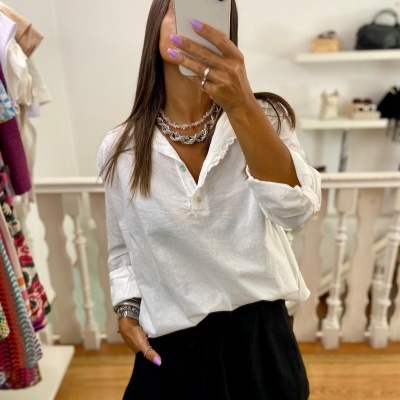 Mulher a tirar selfie com camisa branca e calções pretos em loja de roupa.