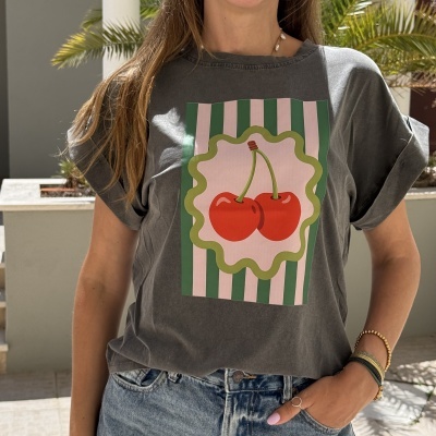 T-shirt cinza com estampa de cerejas vermelhas e riscas verdes e rosas, usada com jeans e pulseiras.